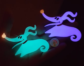 May include: Two glowing Zero figures from The Nightmare Before Christmas. One is teal, the other is purple. Both have a small orange light at the end of their noses and a red collar. A small round sticker is also visible.