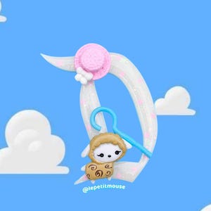 Op de afbeelding: Een grillige illustratie van een schapenkarakter dat aan een halve maan hangt, met een roze hoed en een blauwe hanger. De achtergrond is een helderblauwe lucht met pluizige witte wolken. De tekst "@lepetitmouse" staat onderaan.