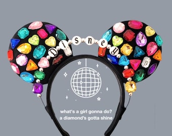 Peut inclure: Bandeau d'oreilles de souris noir avec des strass multicolores et le mot "DISNEY" écrit en perles argentées. Le bandeau est orné d'un motif de boule disco et du texte "what's a girl gonna do? a diamond's gotta shine".