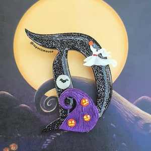 May include: A black glittery letter "D" with a white ghost, a purple witch hat with jack-o'-lantern faces, and a bat. The background features a full moon and a spooky landscape, reminiscent of "The Nightmare Before Christmas."