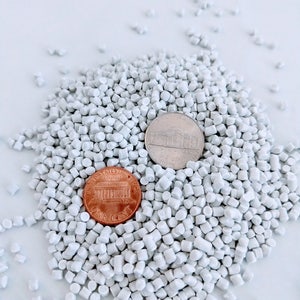 May include: A pile of white plastic pellets with a US penny and a nickel on top.