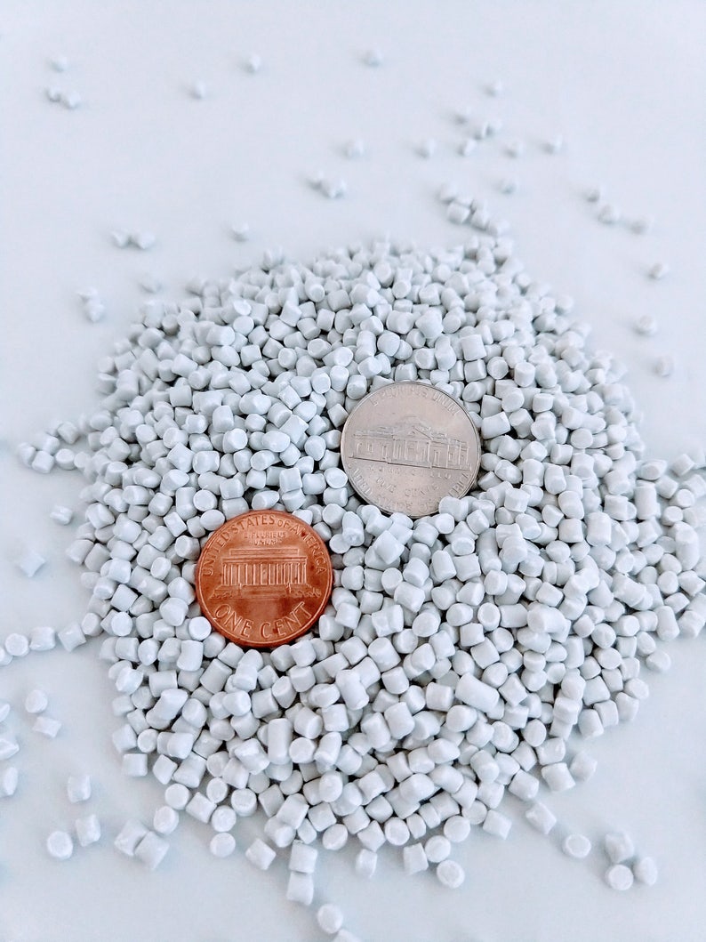 May include: A pile of white plastic pellets with a US penny and a nickel on top.