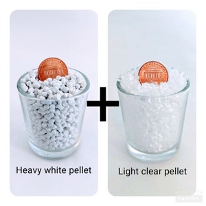 May include: Two glass cups filled with white plastic pellets. The cup on the left contains heavier, opaque white pellets, while the cup on the right contains lighter, translucent clear pellets. A penny is placed on top of the pellets in each cup.