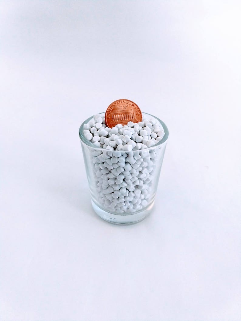 May include: A glass shot glass filled with white plastic pellets with a copper-colored US penny on top.