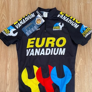 Peut inclure: Maillot de cyclisme noir avec des motifs de clés jaunes, rouges et bleues. Le maillot porte l'inscription "EURO VANADIUM" sur le devant et les manches.