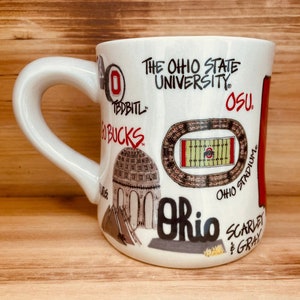 May include: White ceramic mug featuring illustrations and text related to The Ohio State University. The mug includes images of the stadium, a domed building, and the text "Ohio", "OSU", and "Scarlet & Gray".