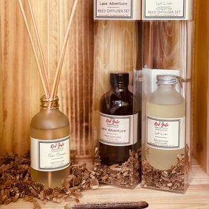 May include: Three glass bottles with reed diffusers in clear boxes. The bottles are labeled "Red Gate Essentials" and have different scents: "Lake Adventure", "Lush Linen", and "Rain Shower".
