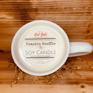 May include: White ceramic mug candle with a label that reads "Red Gate Essentials" and "Pumpkin Souffle Soy Candle". The label also includes the text "Remove Before Burning", "Redgateessentials.com", "1502/425gr", and "Hand Poured in Spartanburg, SC".