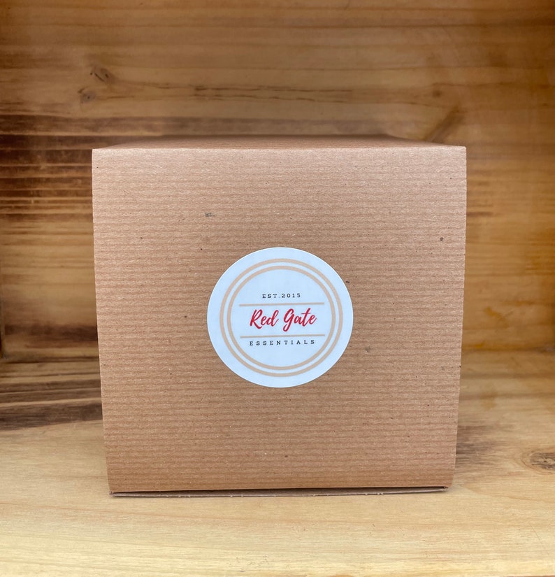 May include: A brown cardboard box with a circular label. The label reads "Red Gate Essentials" in red text, with "Est. 2015" above. The box is square and sits on a wooden surface. The overall aesthetic is simple and rustic.