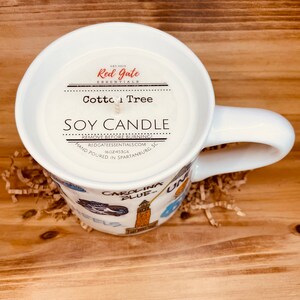 Peut inclure: Une tasse en c&eacute;ramique blanche remplie d'une bougie de soja. La bougie est &eacute;tiquet&eacute;e "Cotton Tree" et "Soy Candle". La tasse a une anse et est d&eacute;cor&eacute;e d'images de Carolina Blue. La bougie p&egrave;se 453 grammes.