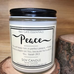 May include: A white soy candle with a black lid and a label that reads "Red Gate Essentials Peace" and a Bible verse from Isaiah 26:3. The candle is handmade in Spartanburg, South Carolina and weighs 7.5 ounces.