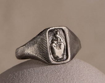 May include: A silver signet ring with a raised design of a hand making a peace sign.