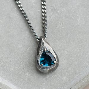 May include: A silver chain necklace with a teardrop-shaped pendant featuring a blue gemstone.