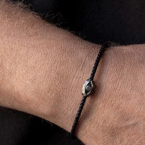 Stylish men's bracelet with black leather band and oxidized sterling silver evil eye centerpiece, showcasing a brutalist design.