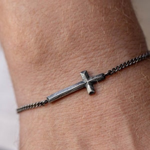 May include: A silver chain bracelet with a small, textured cross pendant.