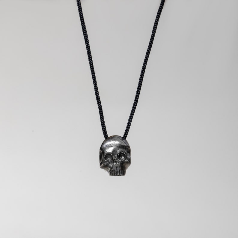 Brutalist skull pendant for men in dark sterling silver. The pendant is made by hand and it is hanging on black cord.