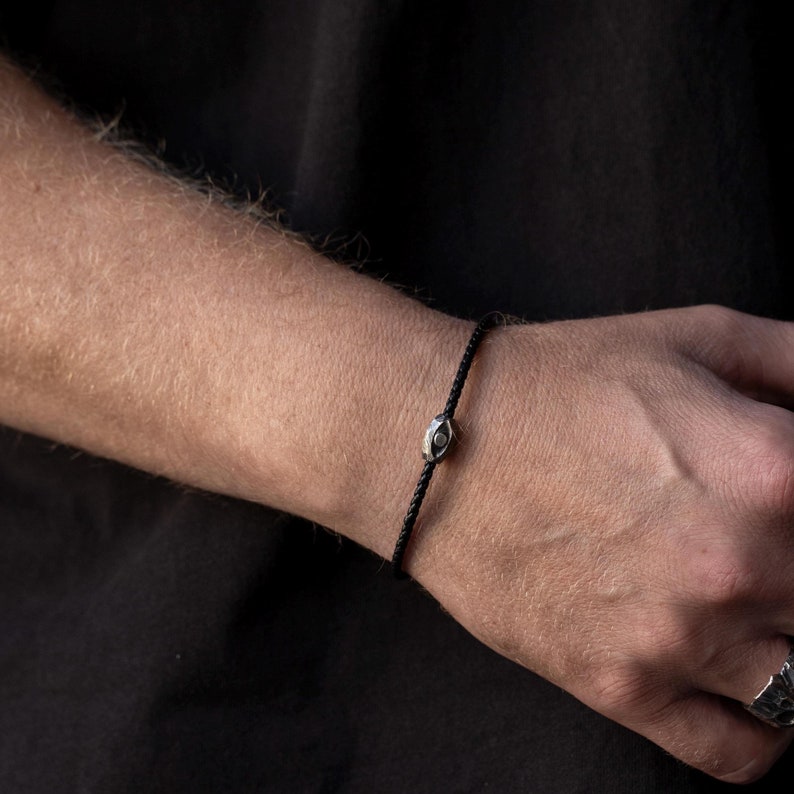 Stylish men's bracelet with black leather band and oxidized sterling silver evil eye centerpiece, showcasing a brutalist design.
