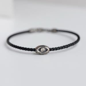 Men's bracelet combining black leather with a raw, brutalist oxidized sterling silver evil eye for a striking and fashionable look