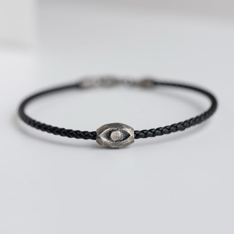 Men's bracelet combining black leather with a raw, brutalist oxidized sterling silver evil eye for a striking and fashionable look