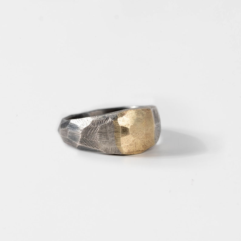 Side view of a brutalist ring handmade of oxidized silver and 14K solid gold. The ring has a tapered faceted band and the blend of gold and silver is obvious.