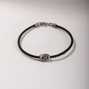 Bold men's bracelet made of black leather and oxidized sterling silver, featuring a distinctive evil eye element in a brutalist aesthetic