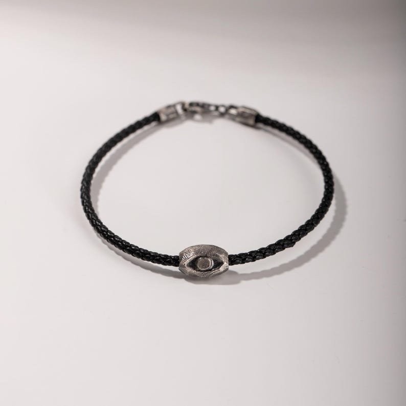 Bold men's bracelet made of black leather and oxidized sterling silver, featuring a distinctive evil eye element in a brutalist aesthetic