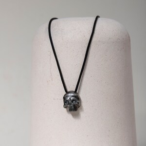 Hand carved skull pendant in oxidized sterling silver. The small pendant is hanging on a black synthetic cord.