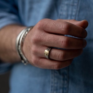 Faceted silver and gold ring for men, worn on the ring finger of a male model.