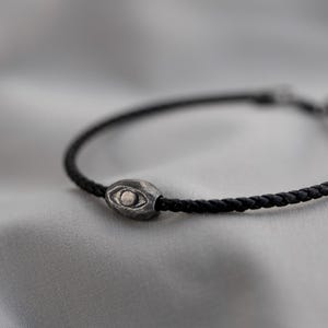 Modern men's bracelet with black leather strap and oxidized sterling silver evil eye symbol in a raw, brutalist design