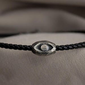 An edgy men's bracelet made from black leather with an oxidized sterling silver evil eye detail, embodying a brutalist design element.