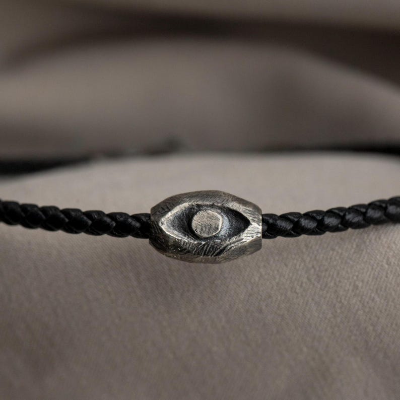 An edgy men's bracelet made from black leather with an oxidized sterling silver evil eye detail, embodying a brutalist design element.
