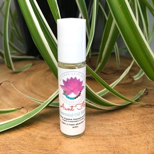 May include: A white roller bottle with a pink lotus flower and the text "NATURES LOVE SHOP MIND BODY SOUL Aunt Flow Essential Oil Blend Grapefruit, Geranium and Organic Fractionated Coconut Oil Apply to lower abdomen or ankle."