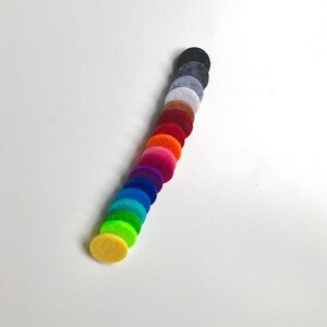 May include: A set of 17 round felt discs in various colours, including yellow, green, blue, purple, pink, orange, red, brown, grey, and black. The discs are arranged in a vertical line, with the yellow disc at the bottom and the black disc at the top.