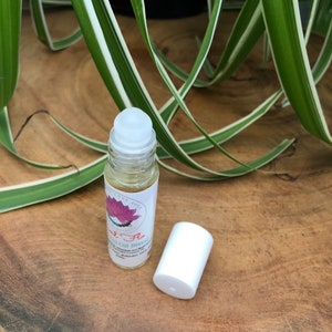 May include: A clear glass roller bottle with a white cap and a pink and white label that says "Soul Flo" Essential Oil Blend. The bottle is sitting on a wooden surface.
