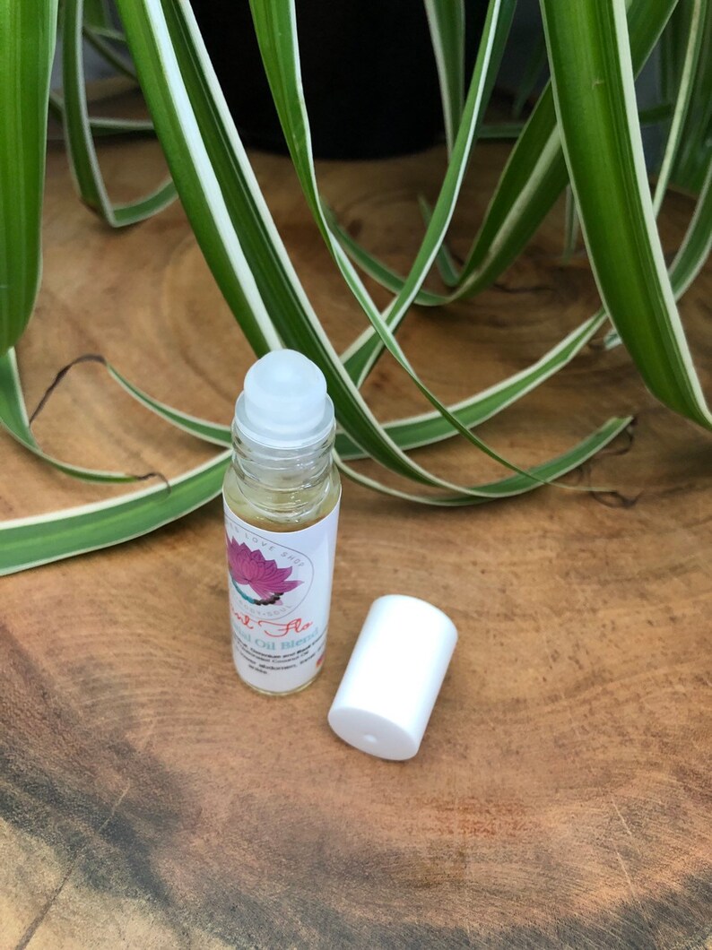 May include: A clear glass roller bottle with a white cap and a pink and white label that says "Soul Flo" Essential Oil Blend. The bottle is sitting on a wooden surface.