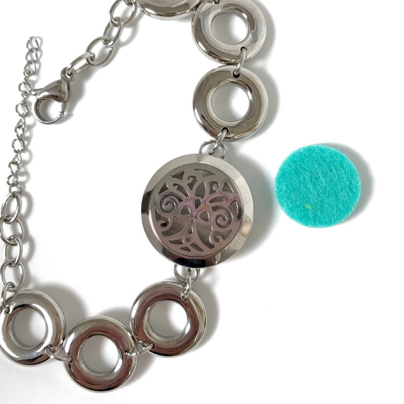 May include: A silver bracelet with a round, openwork charm and a chain. The bracelet has several round links. A turquoise felt pad is also shown.