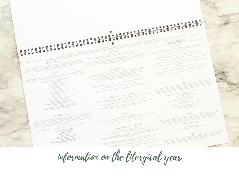 May include: A white spiral-bound calendar open to a page with detailed text. The text is arranged in columns and blocks, with the words "information on the liturgical year" at the bottom. The calendar is on a light-colored surface.