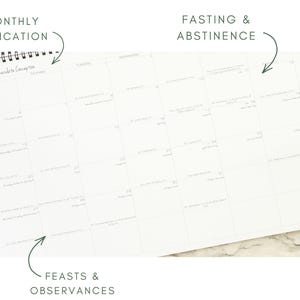 May include: A white spiral-bound calendar with a grid layout. The calendar is open to a month with handwritten entries. Text at the top reads "Monthly Dedication" and "Fasting & Abstinence." The bottom reads "Feasts & Observances."