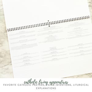 May include: A white spiral-bound calendar open to a page with text. The text is organized into rectangular blocks. The bottom of the image has the text "catholic living appendixes" and "favorite catholic prayers, papal intentions, liturgical explanations."