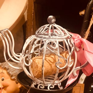 May include: White metal wire bottle stopper shaped like a teapot with a cork inside. The stopper has a pink ribbon attached to it.