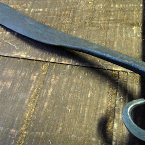 May include: A hand-forged metal tool with a curved handle and a sharp blade. The tool is made of dark blue metal and has a rustic finish.