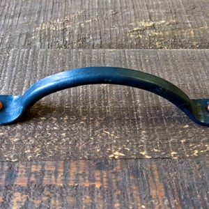 May include: Black metal drawer pull with a curved handle and copper accents. The pull has a simple, rustic design.