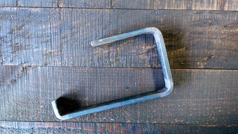 May include: A metal shelf bracket with a simple, industrial design. The bracket is made of sturdy metal and has a raw, unfinished look.
