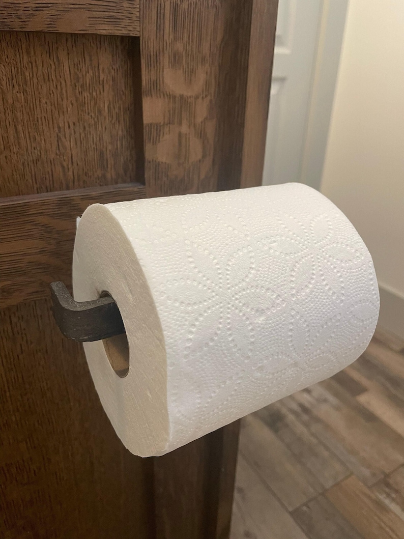 May include: A white toilet paper roll on a black metal toilet paper holder attached to a wooden door.