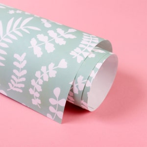 May include: A roll of green wrapping paper with a white leaf pattern. The paper is rolled up and the end is visible.
