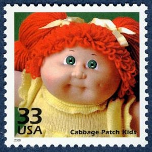 May include: A 33 cent USA postage stamp featuring a Cabbage Patch Kids doll with red yarn hair, green eyes, and a yellow dress.