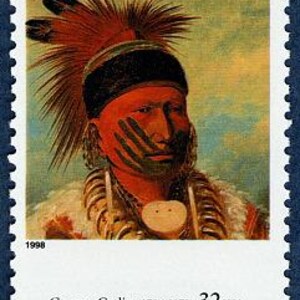 May include: A vintage postage stamp featuring a portrait of a Native American man with a feathered headdress, painted in red, black, and white. The stamp is from 1998 and features the text "George Catlin (1796-1872) 32¢ USA".