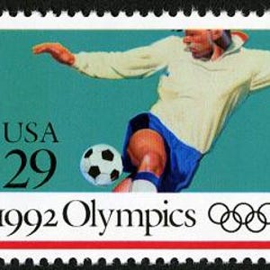 Puede incluir: Un sello postal de 29 centavos con un jugador de f&uacute;tbol pateando un bal&oacute;n. El sello es azul, blanco y negro con el texto "USA 29" y "1992 Olympics" con los anillos ol&iacute;mpicos.