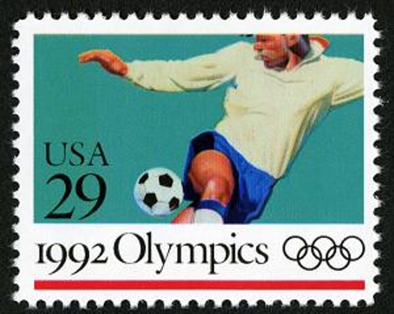 Puede incluir: Un sello postal de 29 centavos con un jugador de f&uacute;tbol pateando un bal&oacute;n. El sello es azul, blanco y negro con el texto "USA 29" y "1992 Olympics" con los anillos ol&iacute;mpicos.