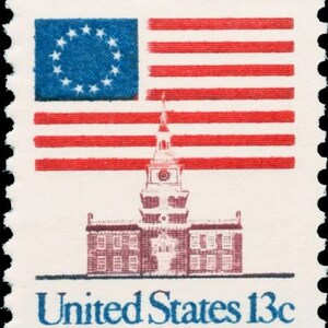 Puede incluir: Un sello postal estadounidense vintage que presenta una bandera estadounidense roja, blanca y azul con 13 estrellas, un edificio con una torre de reloj y el texto "United States 13c".